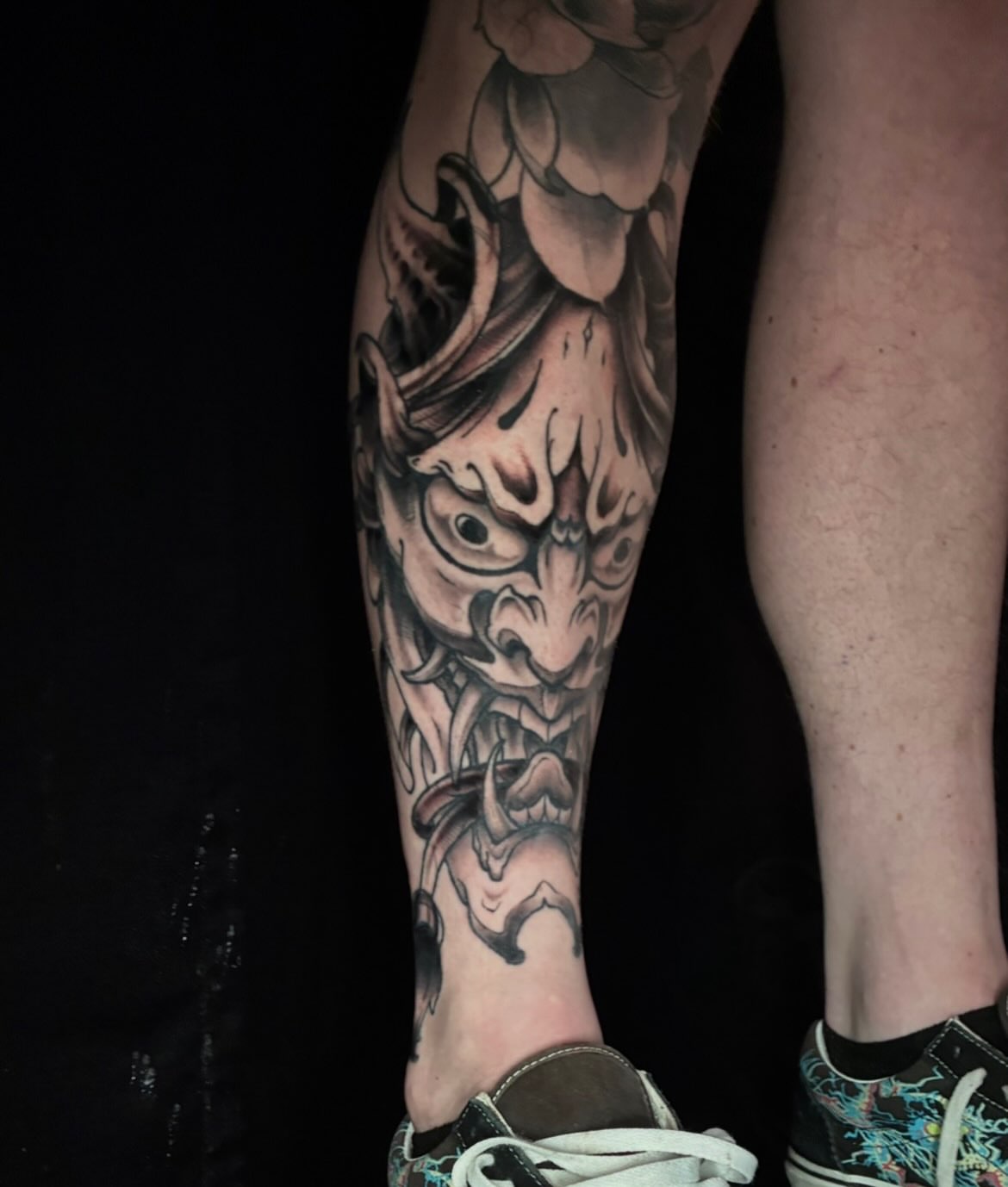 Demon mask black and grey tattoo on the calf by Alex Larsen