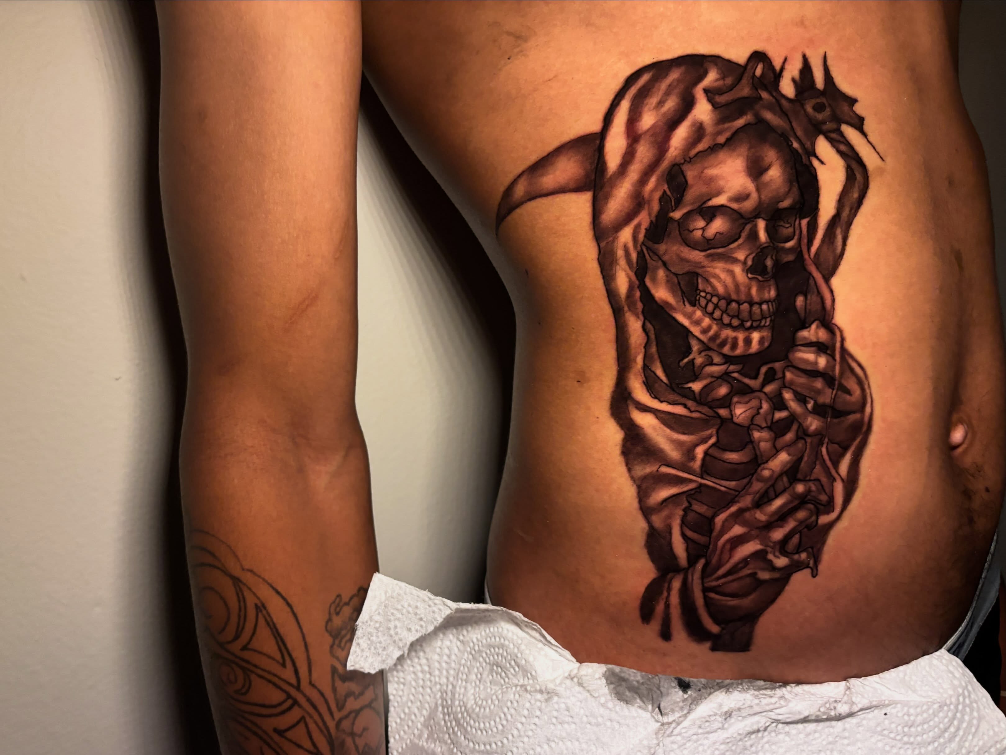 Skull and hooded figure dark realism tattoo on the ribs by Inkys Tatts