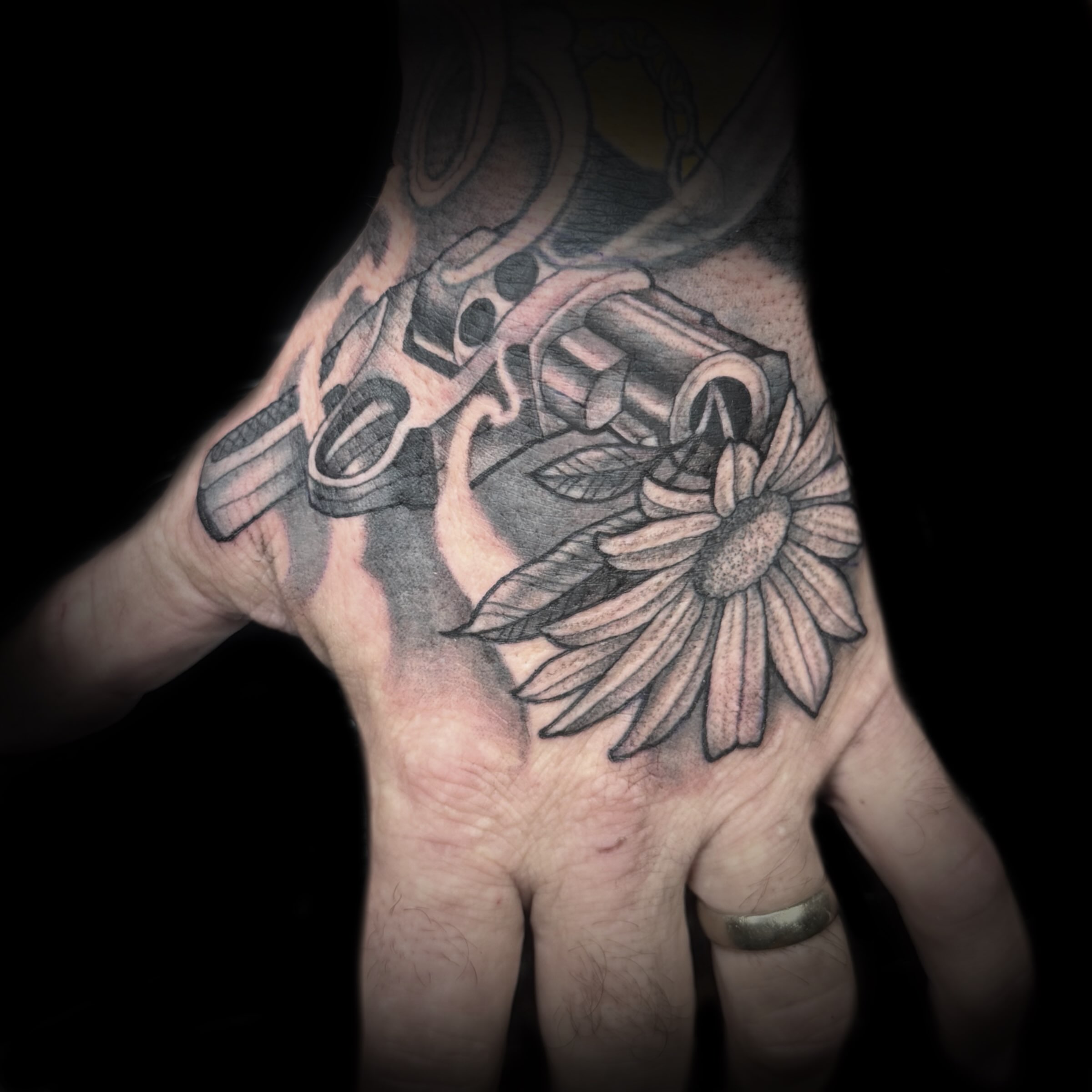 Gun and flower black and grey tattoo on the hand by Kelsea Weir McCree