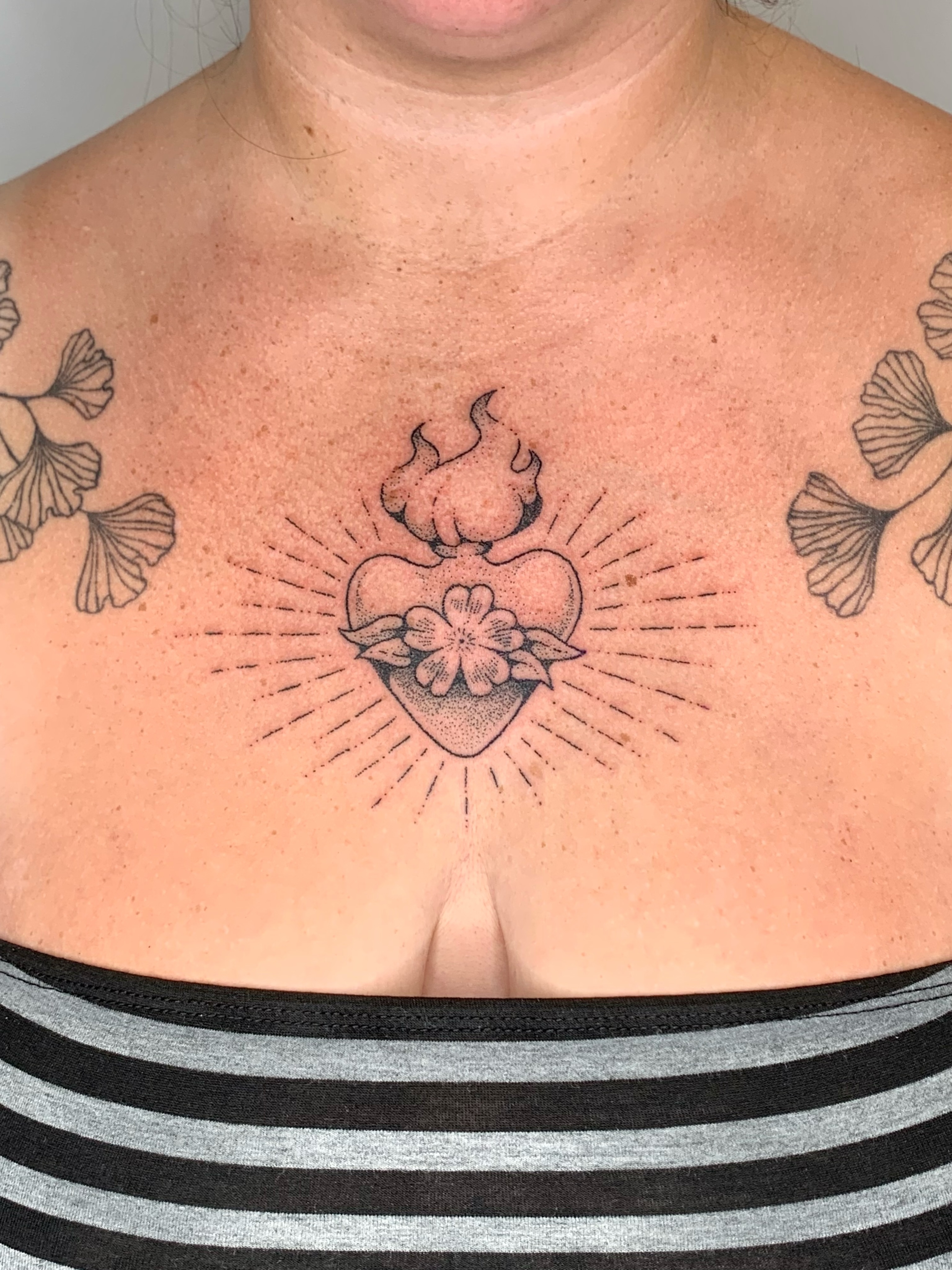 Heart with flames and flower dotwork tattoo on the chest by Lex Lloyd