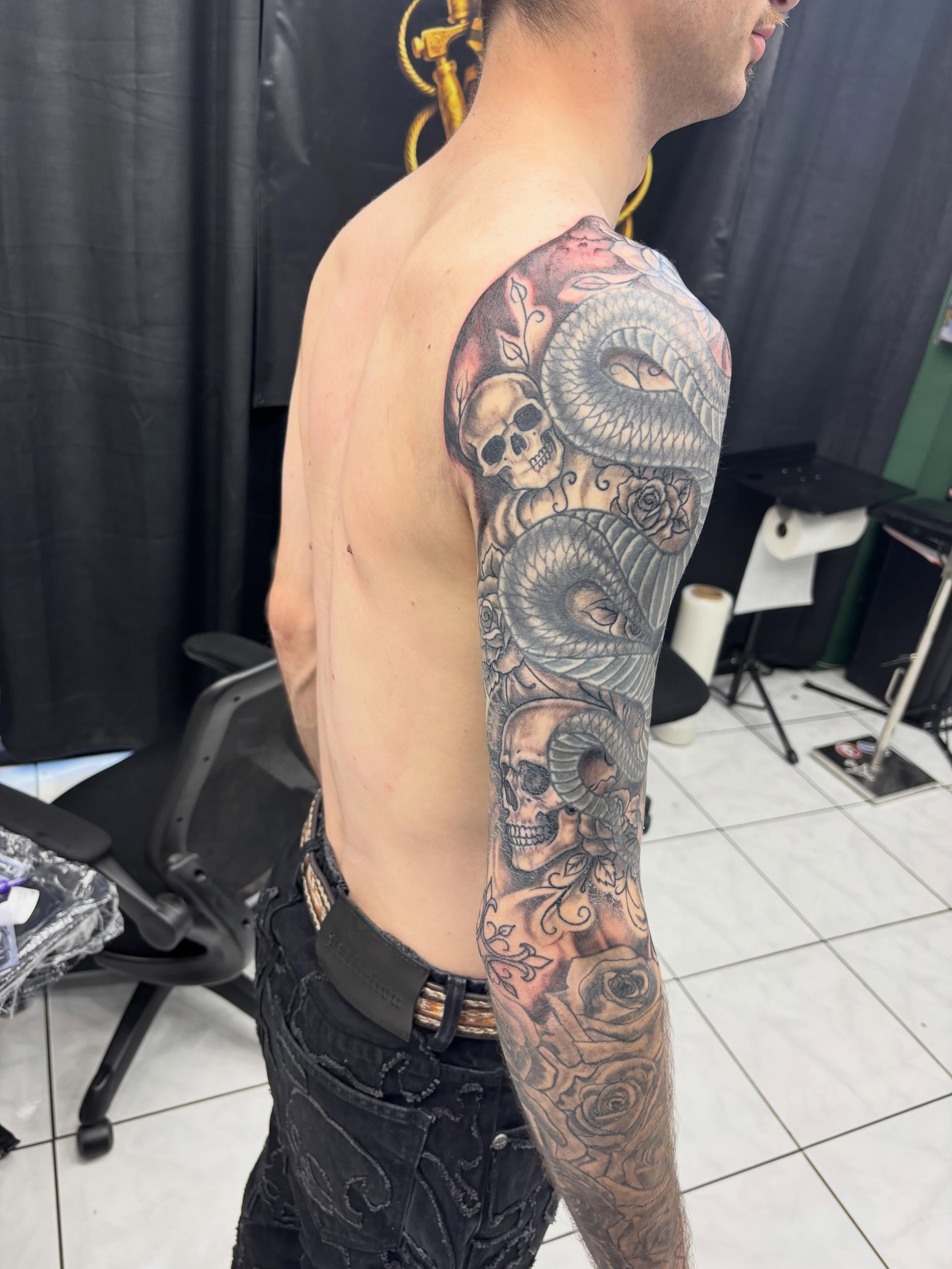 Snake and skull realism tattoo on the upper arm by Shadows Tattoos