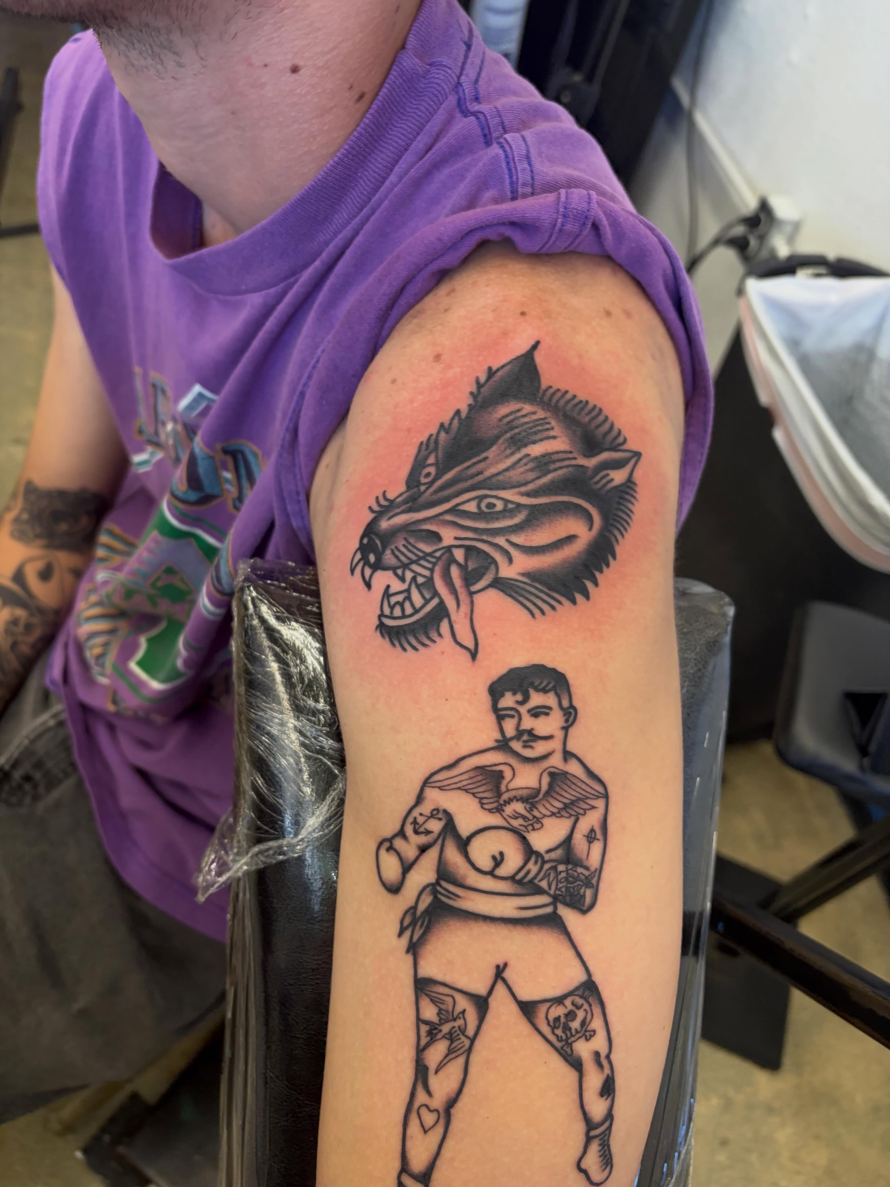 Wolf and man American traditional tattoo on the upper arm by Payton Prentice