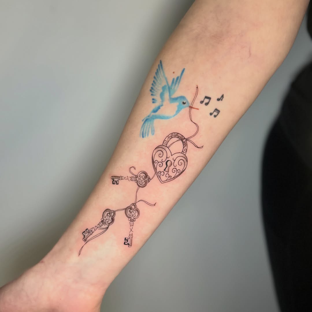 Bird and heart lock fine line tattoo on the forearm by Mandy Kaur