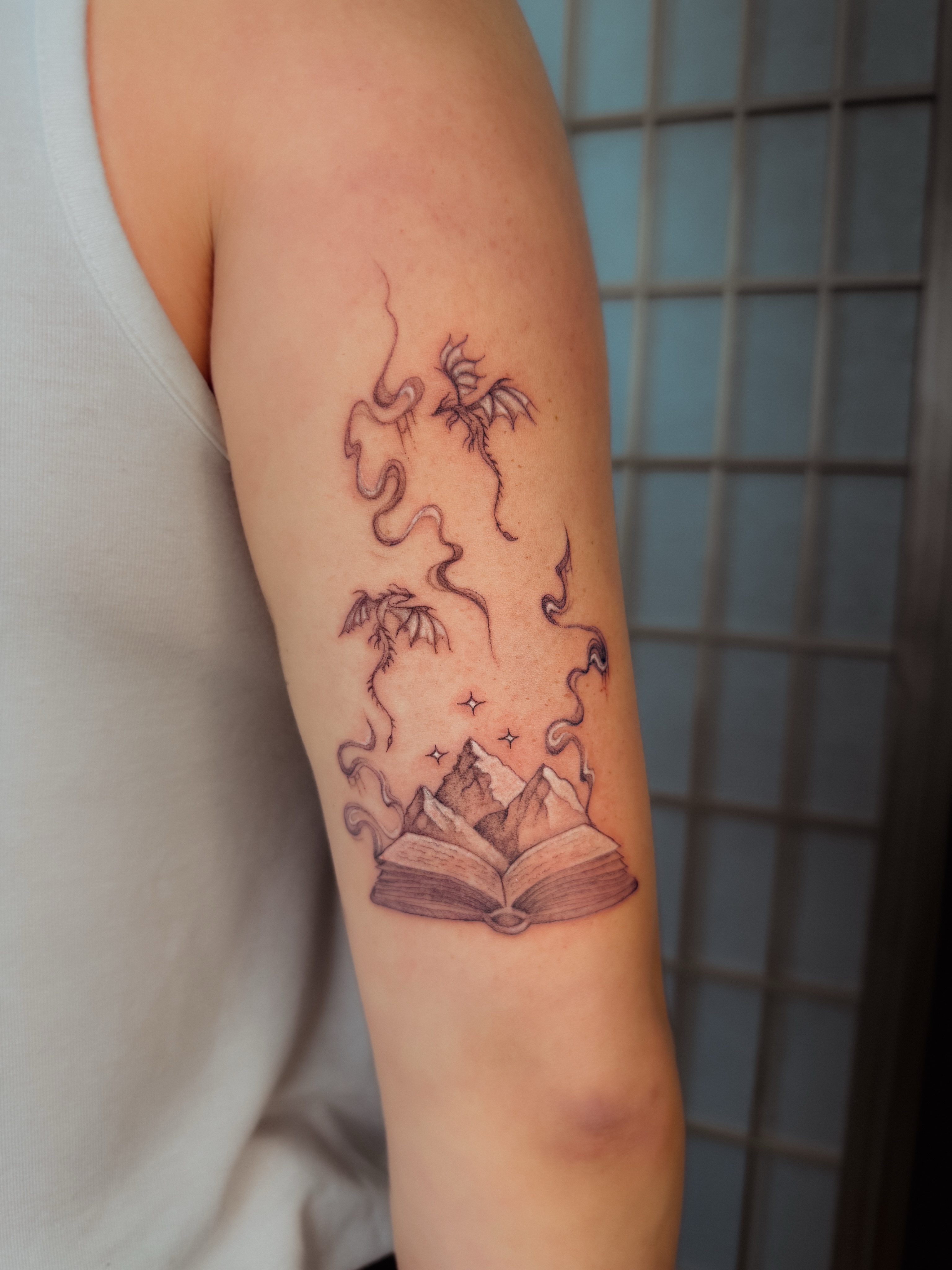 Open book with mountains and dragon dotwork tattoo on the forearm by 𝐇𝐚𝐫𝐩𝐞𝐫