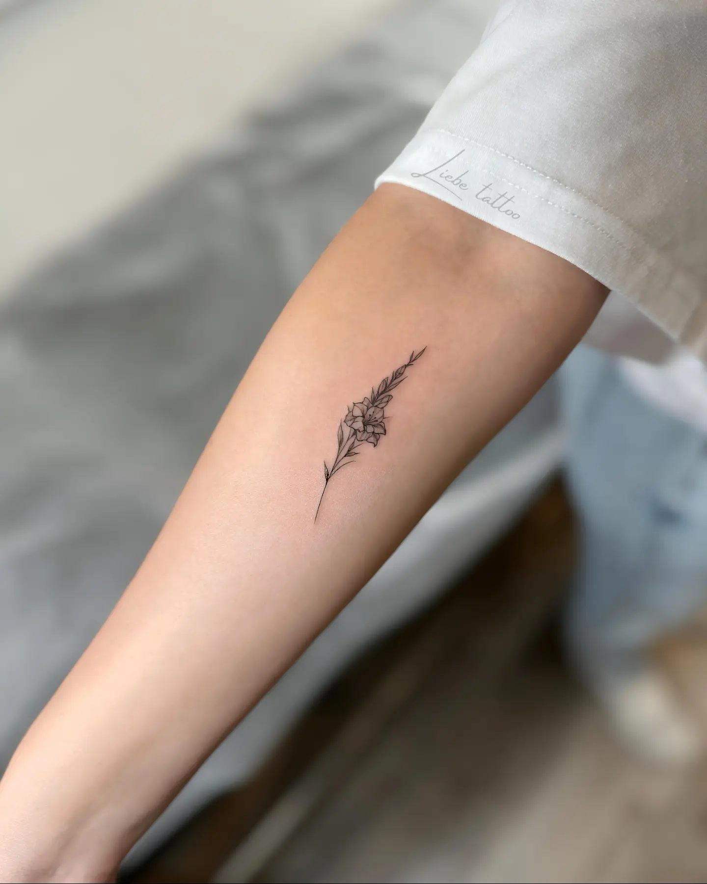 Flower and feather fine line tattoo on the forearm by Floral Fineline Tattoo