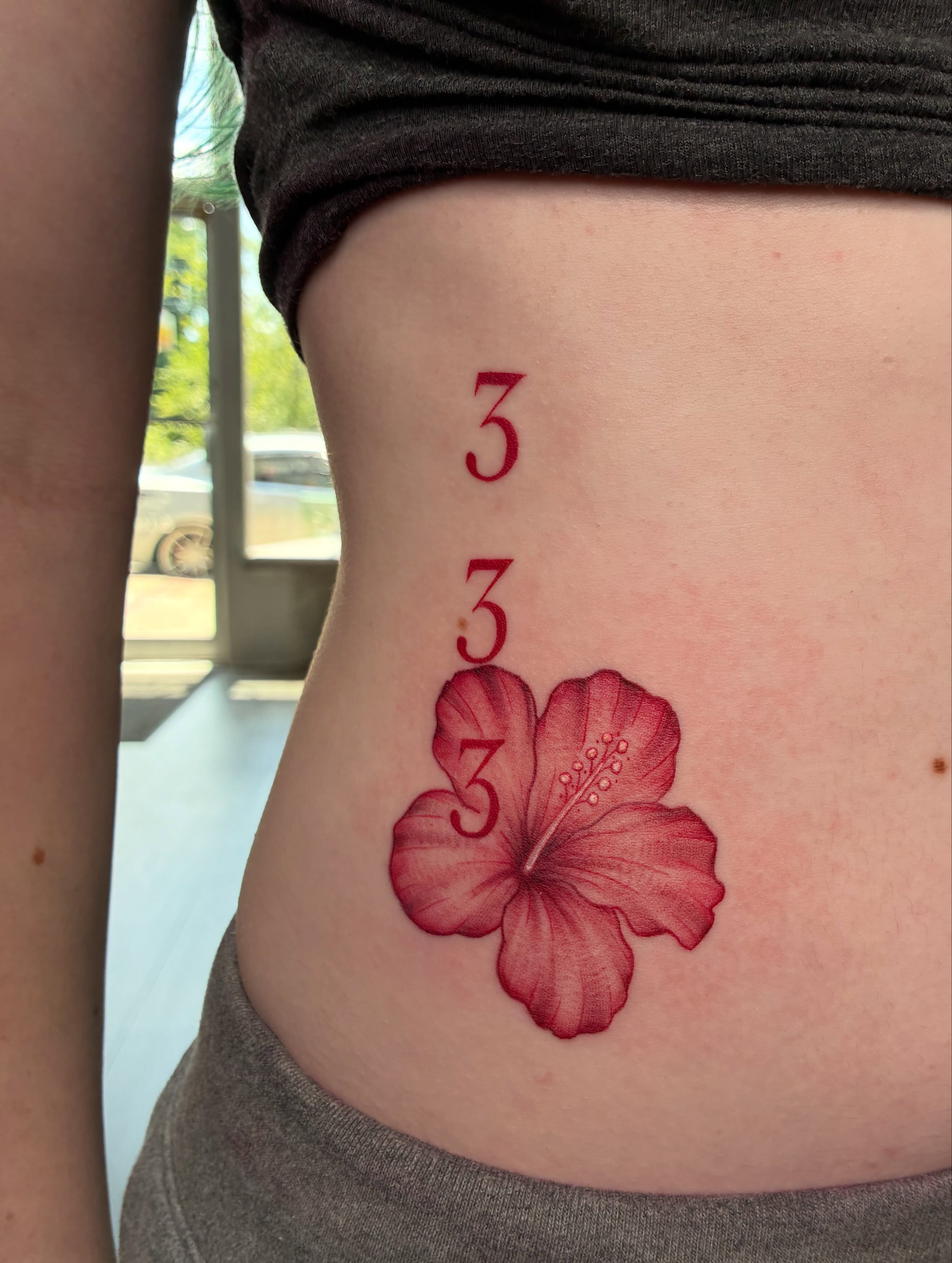 Red hibiscus flower realism tattoo on the torso by Tattoos by Hailey