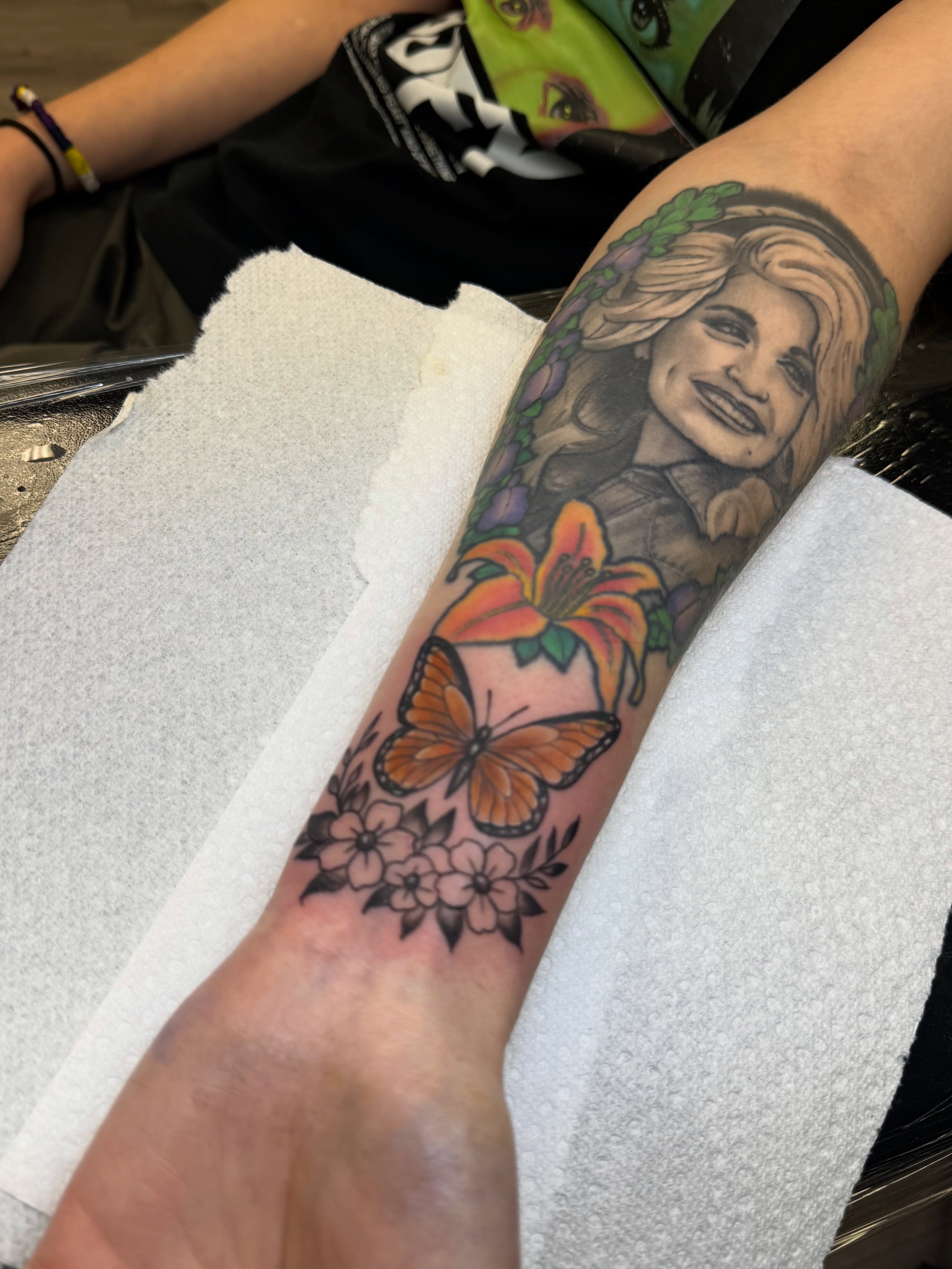 Portrait with flowers and butterfly American traditional tattoo on the forearm by Israel Jacob Woehler