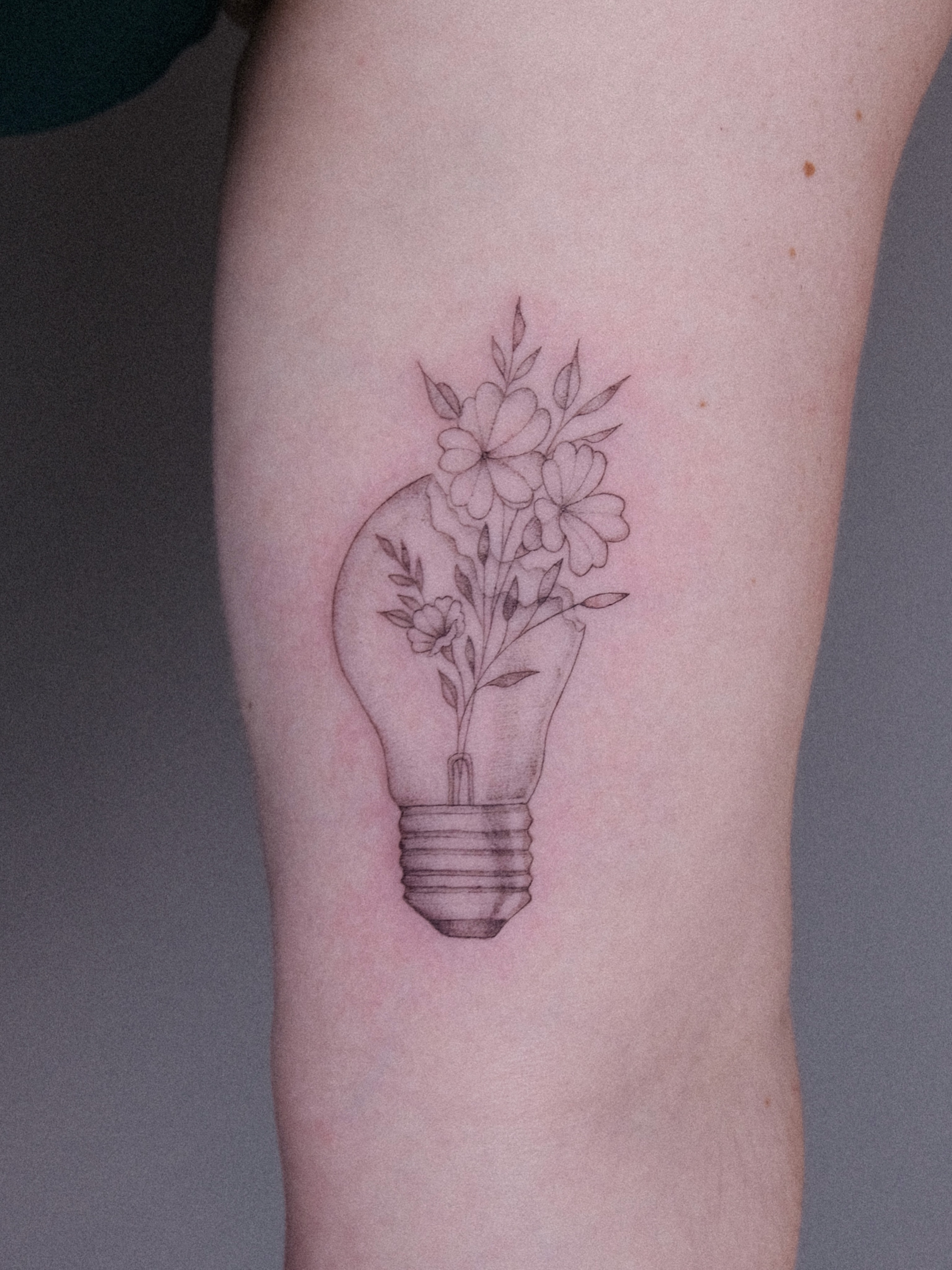 Light bulb with flowers black and grey tattoo on the forearm by Anna