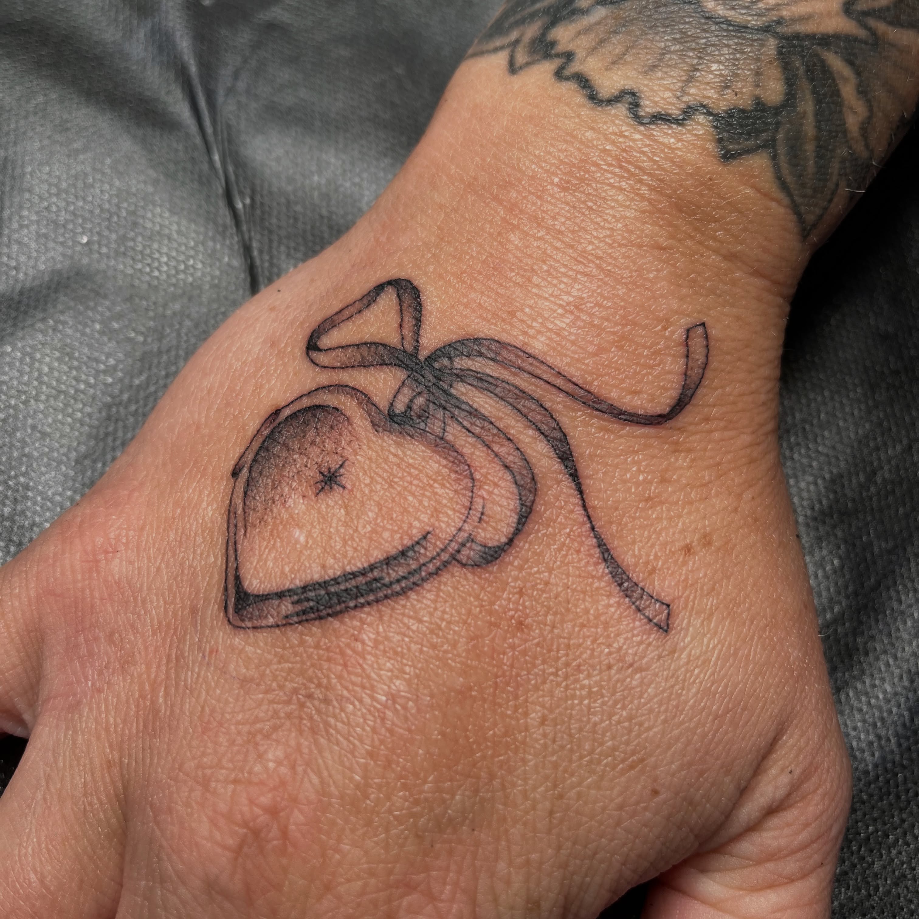 Heart with bow black and grey tattoo on the hand by christina diaz