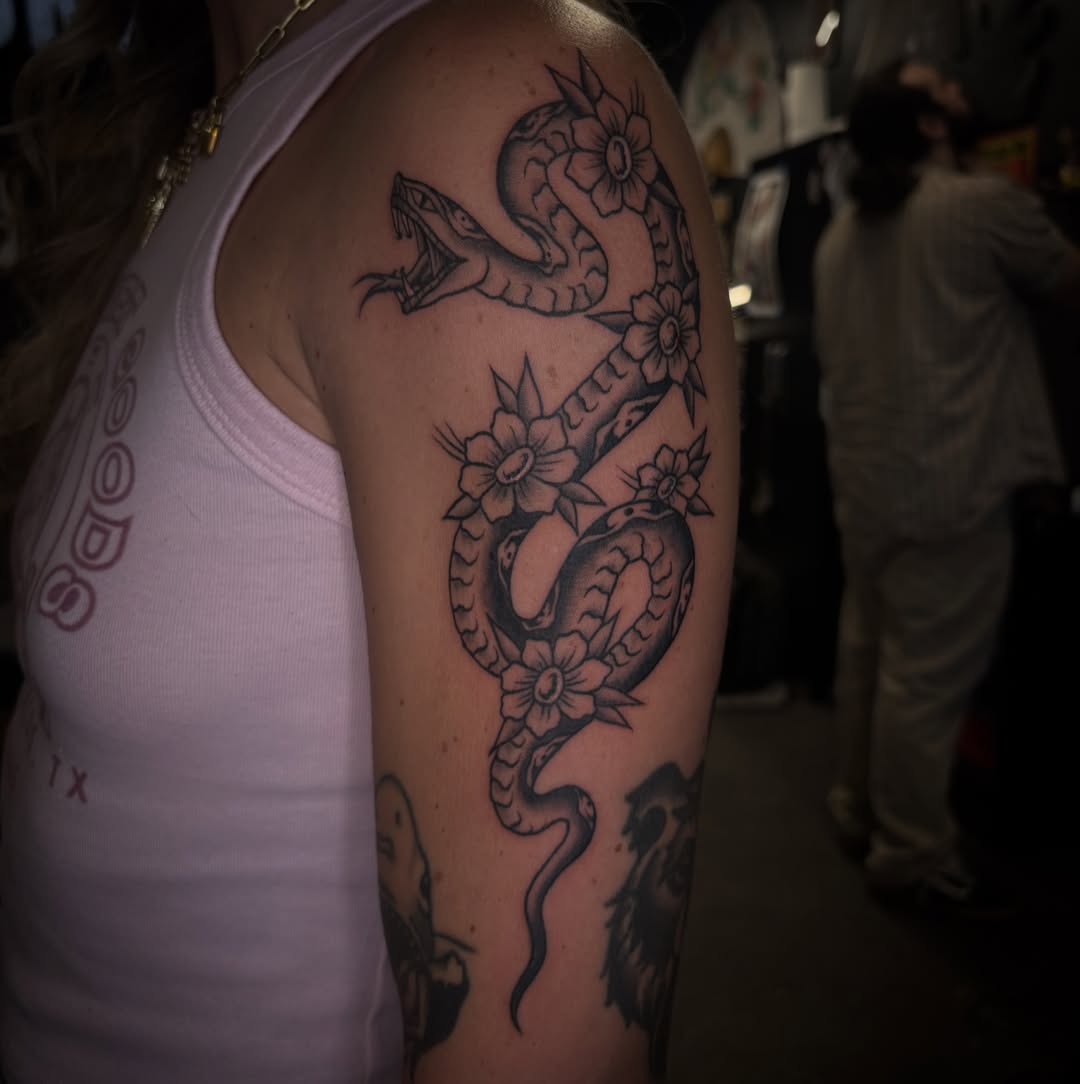 Snake and flowers black and grey tattoo on the upper arm by Brett Ferguson