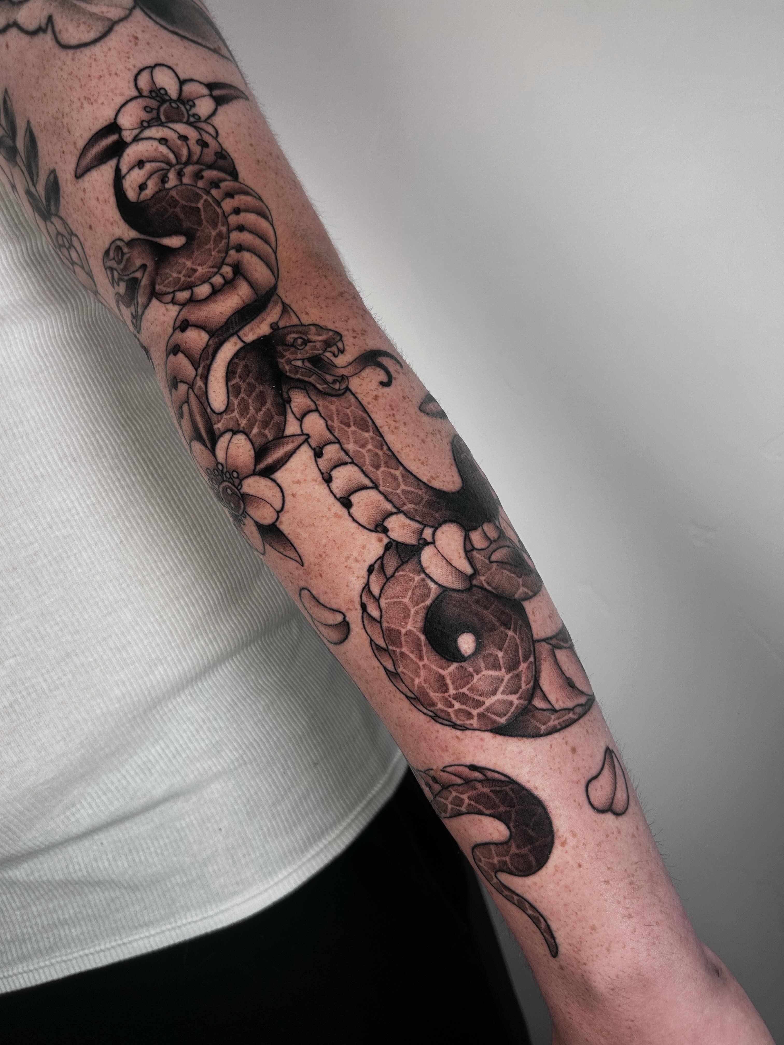 Snake and flowers black and grey tattoo on the forearm by Salt Lake City tattoo artist
