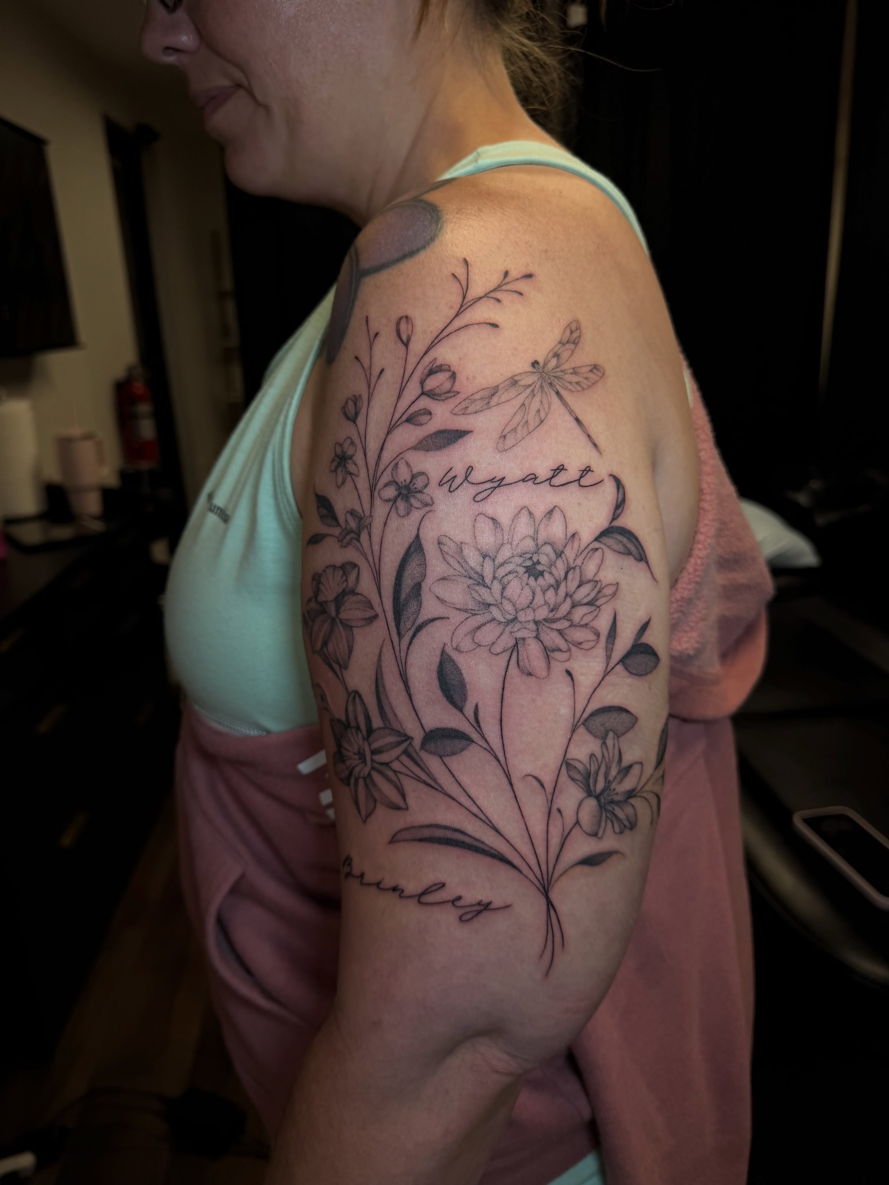 Floral arrangement with dragonfly black and grey tattoo on the shoulder by Priscilla Michels