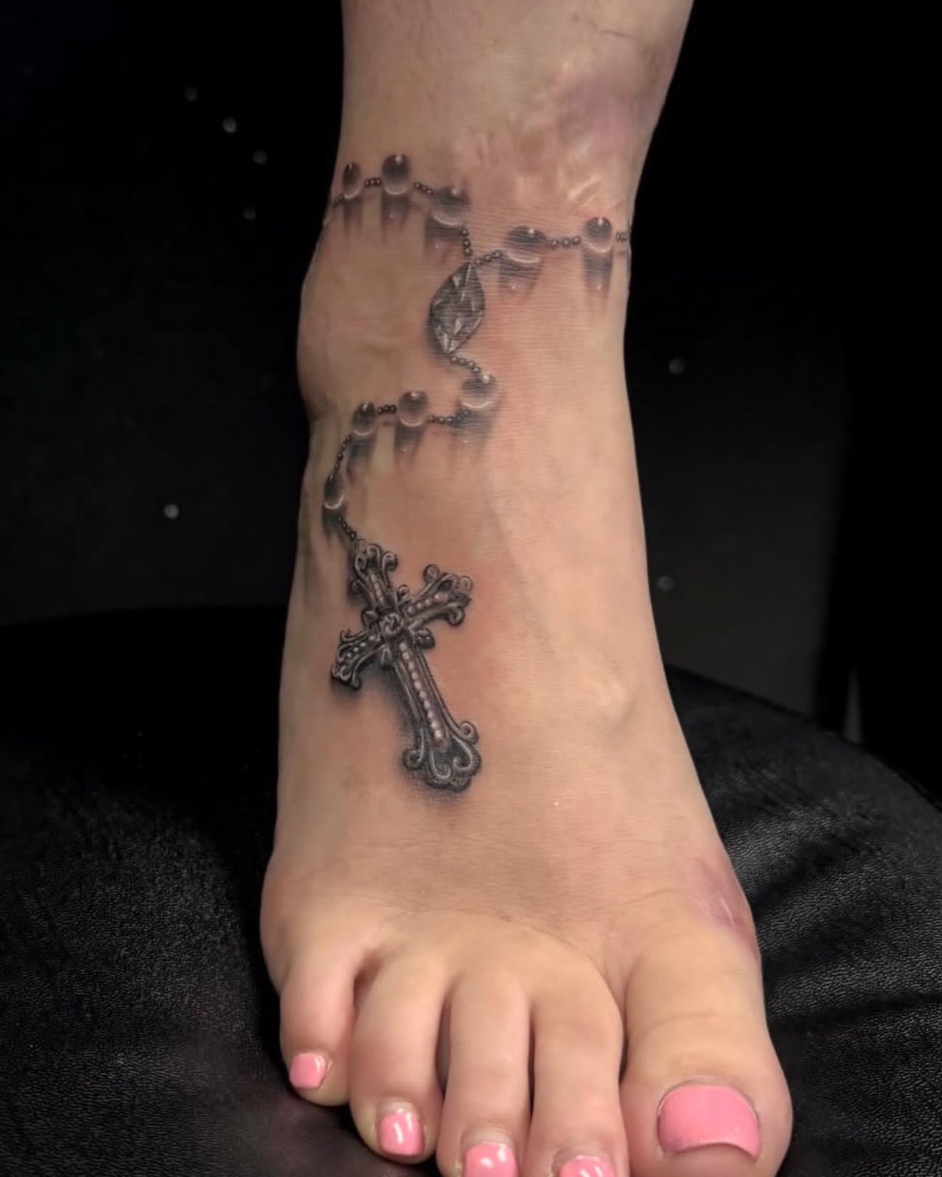 Rosary and cross black and grey tattoo on the foot by Amber Lynn