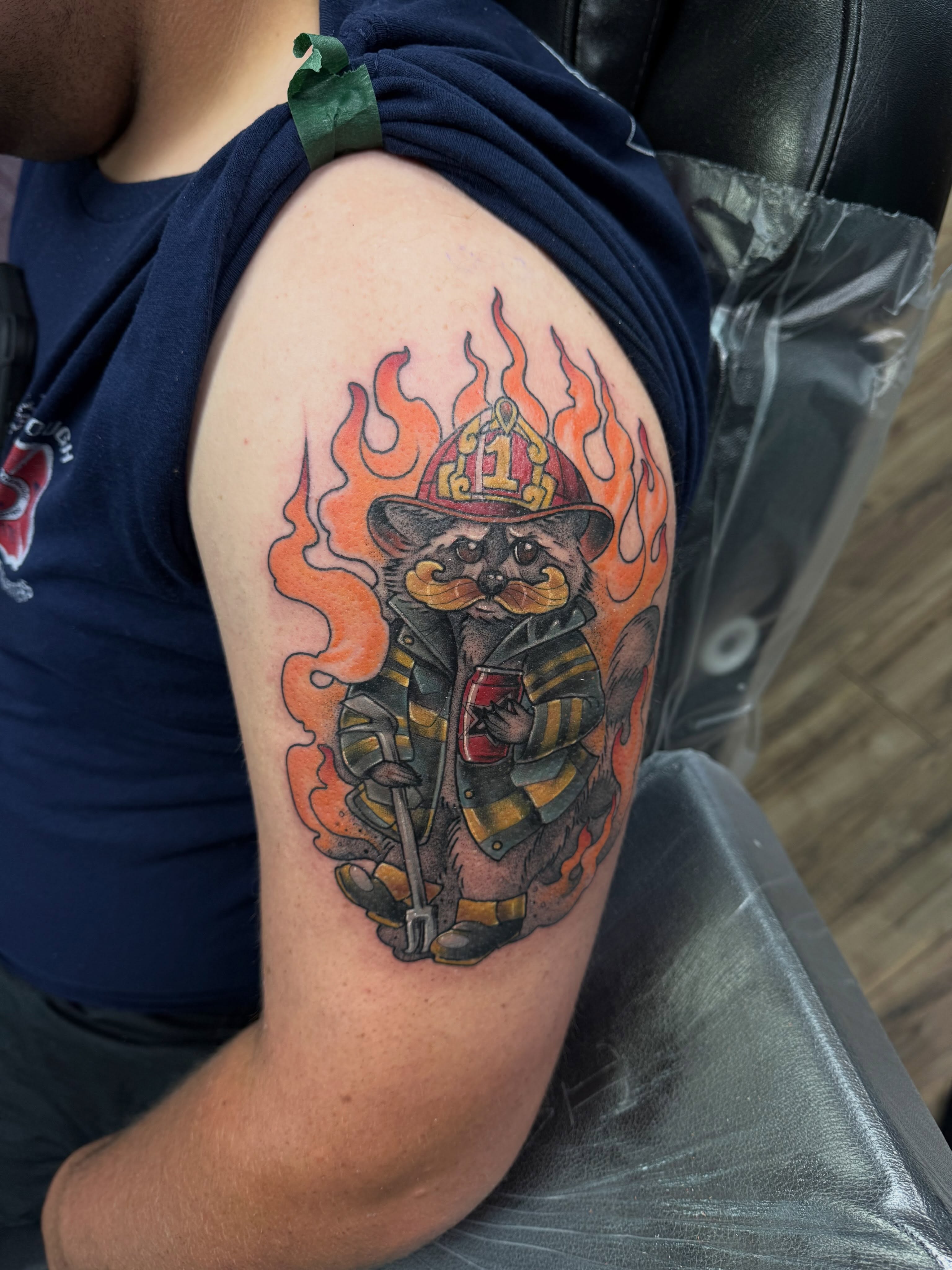 Raccoon firefighter realism tattoo on the upper arm by Eileen Joyce