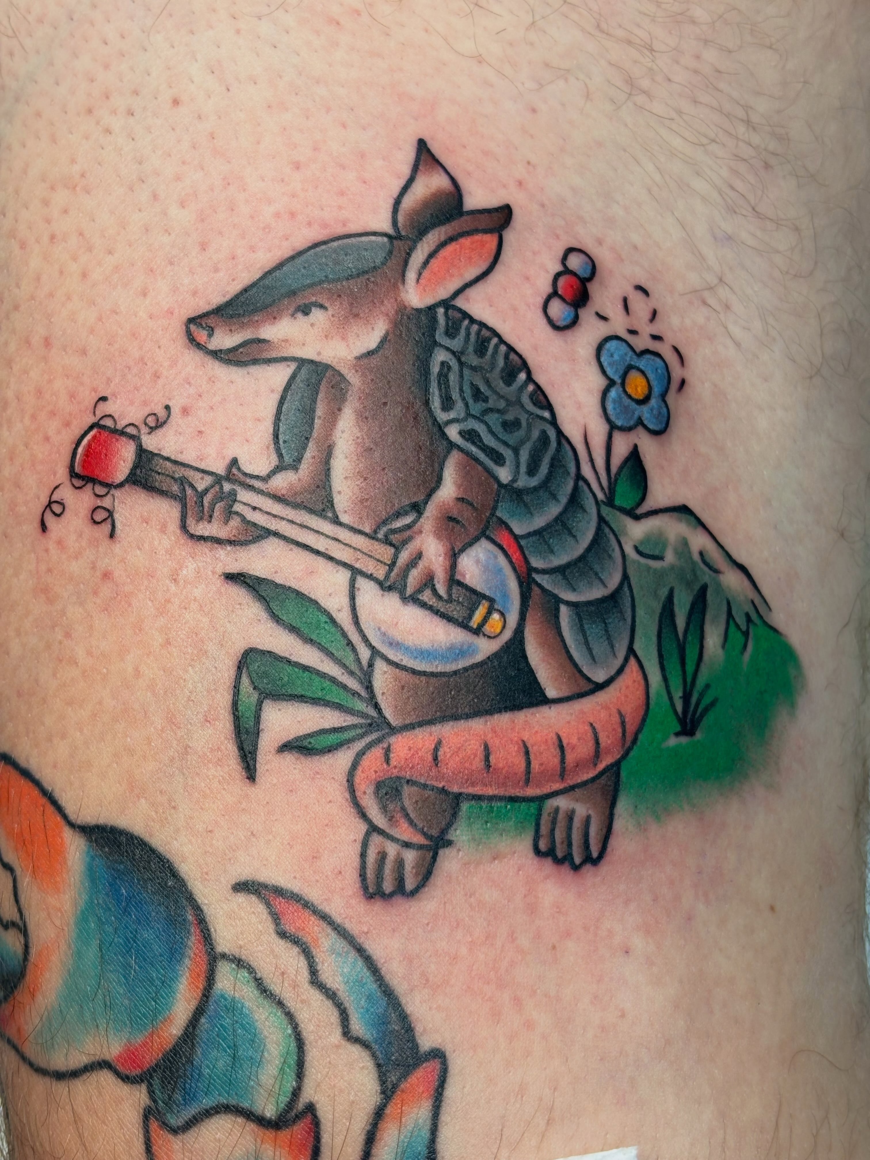 Armadillo playing banjo American traditional tattoo on the thigh by Nick Tate