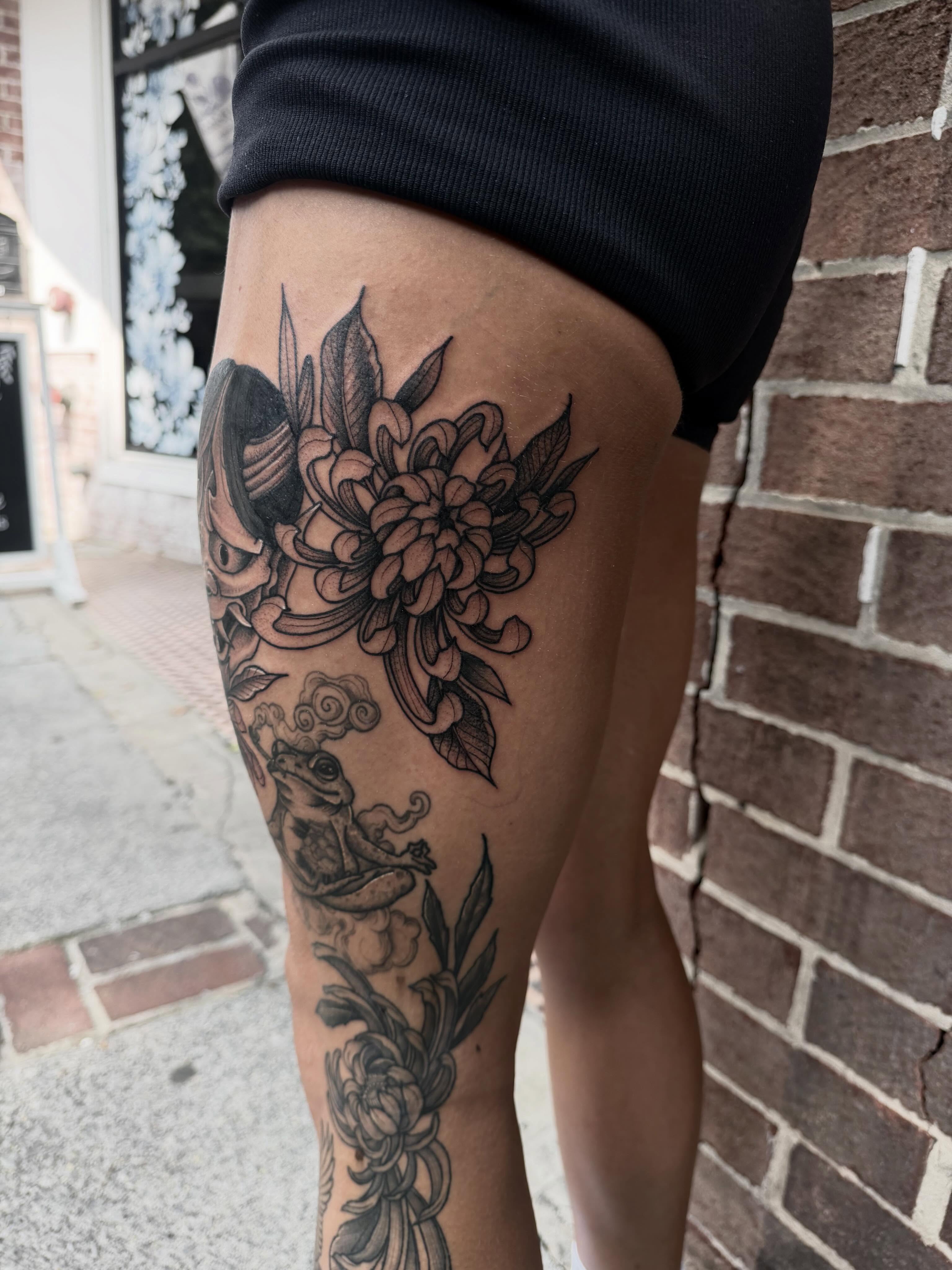 Flower and frog black and grey tattoo on the thigh by Ashleigh Lapole
