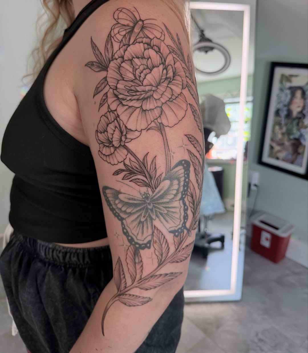 Butterfly and flowers black and grey tattoo on the upper arm by Liz Aulenbacher